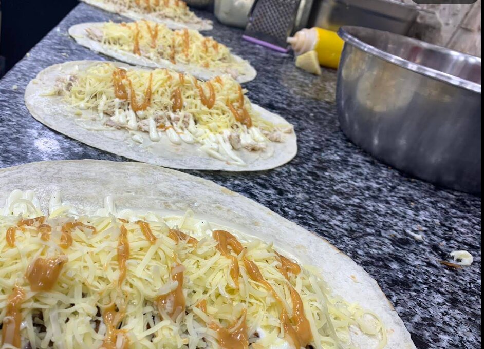 Préparation de tacos garnis de fromage et de sauce chez Mc Bizou